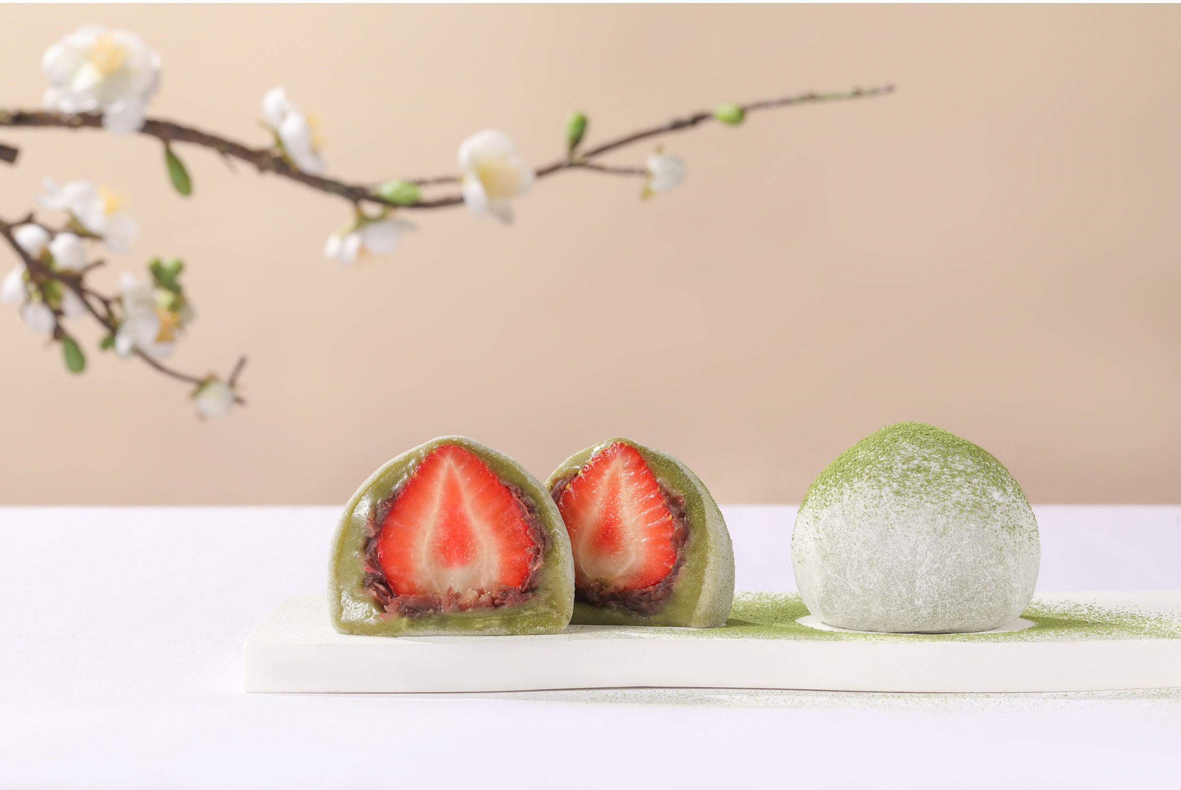Three green tea confections with strawberry filling on a white surface, with a beige background and floral branch.